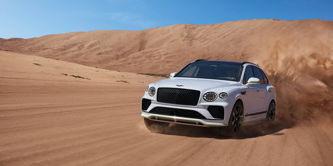 Bentley Brussels Bentley Bentayga Speed SUV front three quarter in Snow Quarts Pearlescent by Mulliner white paint driving dynamically through the desert