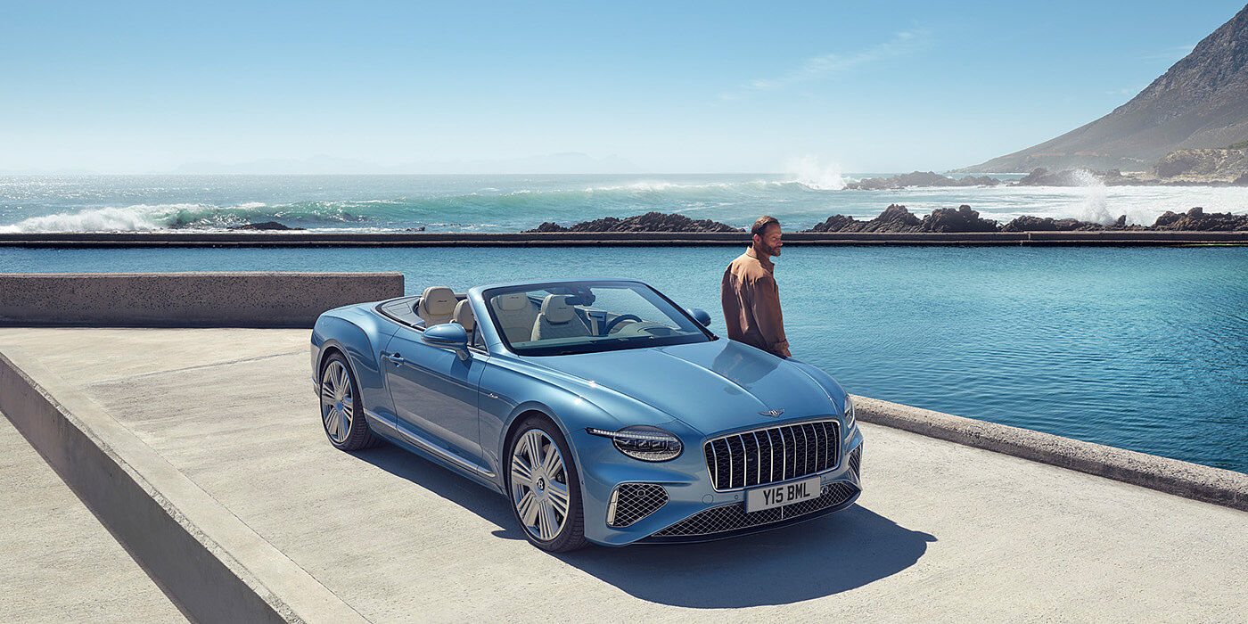 Bentley Brussels New Bentley Continental GTC Azure convertible front view in Light Windsor blue paint with 22 inch ten spoke wheels parked by the sea in the sunshine