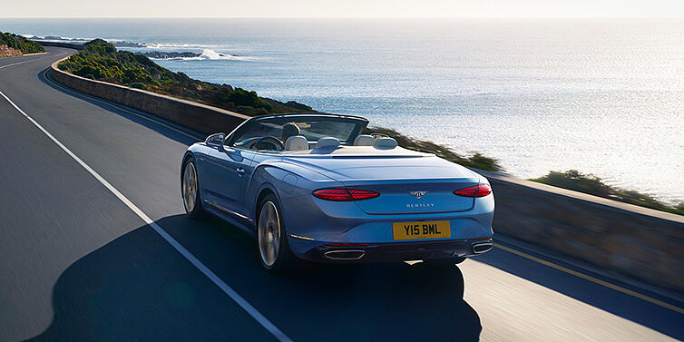 Bentley Brussels New Bentley Continental GTC Azure convertible rear view in Light Windsor blue paint with 22 inch ten spoke wheels driving dynamically on an ocean road in the sunshine