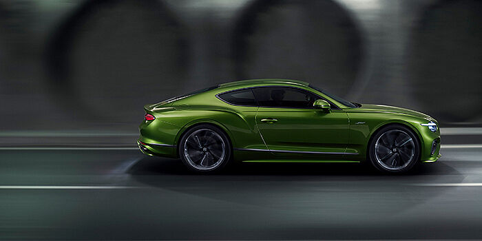  Bentley Brussels Bentley Continental GT coupe in Tourmaline Green paint driving in profile on a dark road