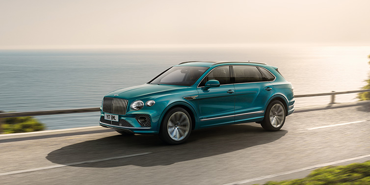 Bentley Brussels Bentley Bentayga Extended Wheelbase Azure SUV in Topaz blue paint driving dynamically by the ocean