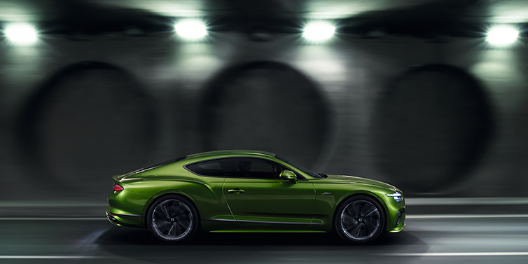 Bentley Brussels Bentley Continental GT Speed coupe profile in Tourmaline Green driving dynamically past a concrete wall at night