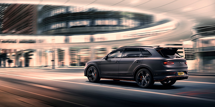 Bentley Brussels Bentley Bentayga S Black Edition SUV rear three quarter in Anthracite Satin paint driving dynamically through a city at night