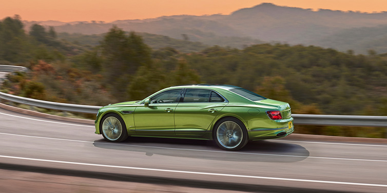 Bentley Brussels Bentley Flying Spur Speed sedan side profile in Tourmaline Green paint driving dynamically on a mountain road at sunset