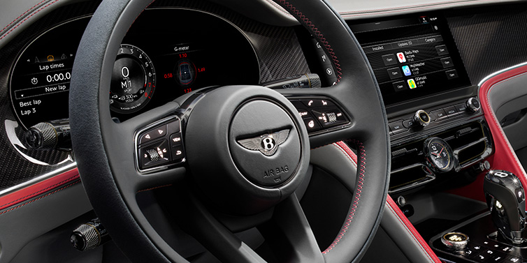 Bentley Brussels Bentley Flying Spur Speed sedan front interior detail showing steering wheel and driver screens surrounded with Hotspur red and Gravity Grey hides